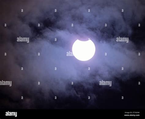 Partial solar eclipse by the moon with clouds in front of the sun ...