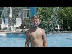 Boy refreshing under waterfall in outside swimming pool