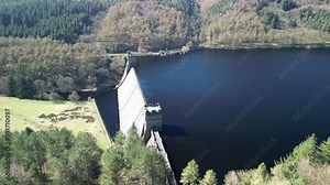 Aerial view of water cascading over the Derwent Dam, in the Peak District, UK with a reveal of the Derwent reservoir towards Howden Reservoir.