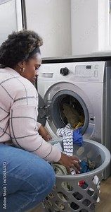 Vertical video of african american woman using washing machine and doing laundry at home